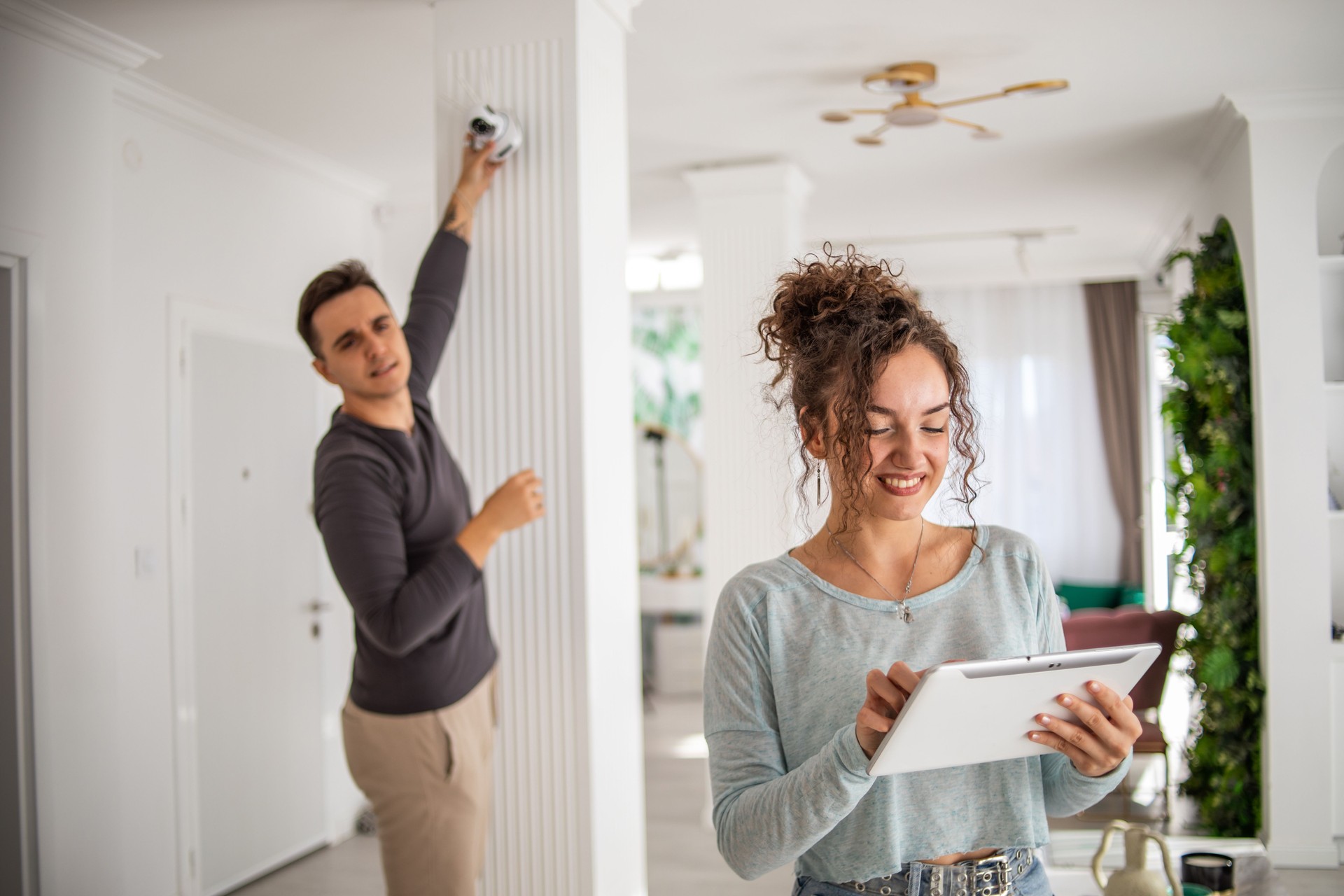 A young couple, a man and a woman, are setting up a security camera for home surveillance in their apartment